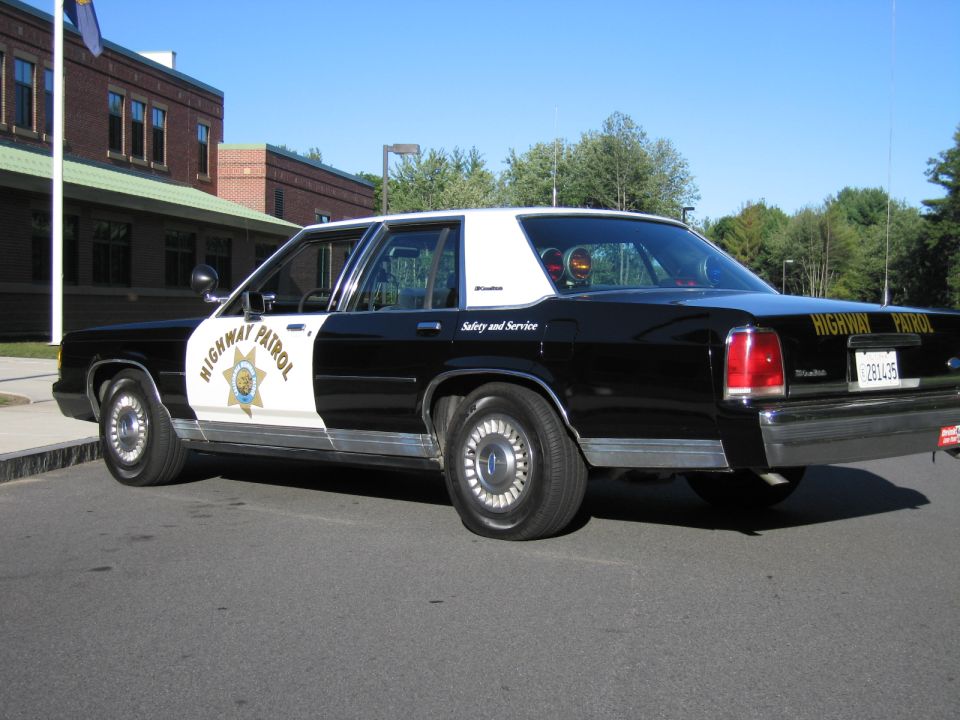 Side view of black-and-white highway patrol sedan with gold star door emblem