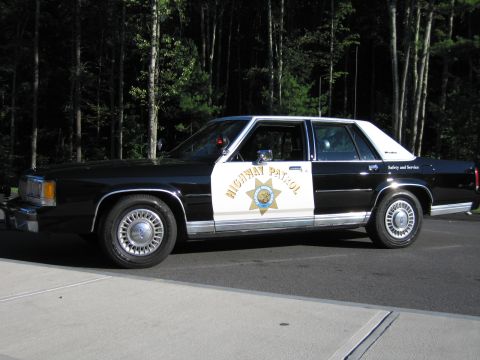 1991 Ford LTD Crown Victoria - Driver-side profile of a black-and-white Ford patrol sedan with HIGHWAY PATROL lettering and a gold star emblem on the front door.