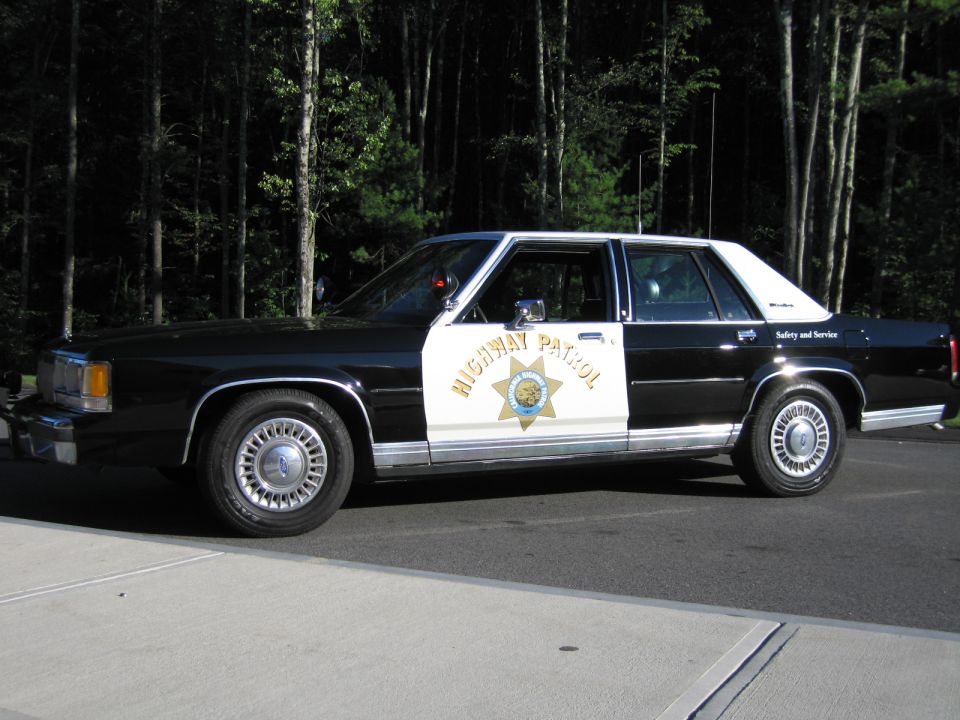 Driver-side profile of black-and-white Ford highway patrol sedan