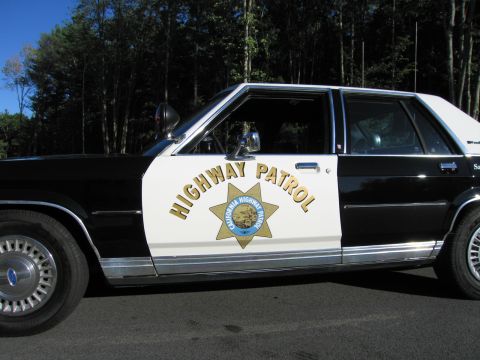 1991 Ford LTD Crown Victoria - Close-up of a black-and-white patrol car door showing HIGHWAY PATROL lettering and a gold California Highway Patrol star emblem.