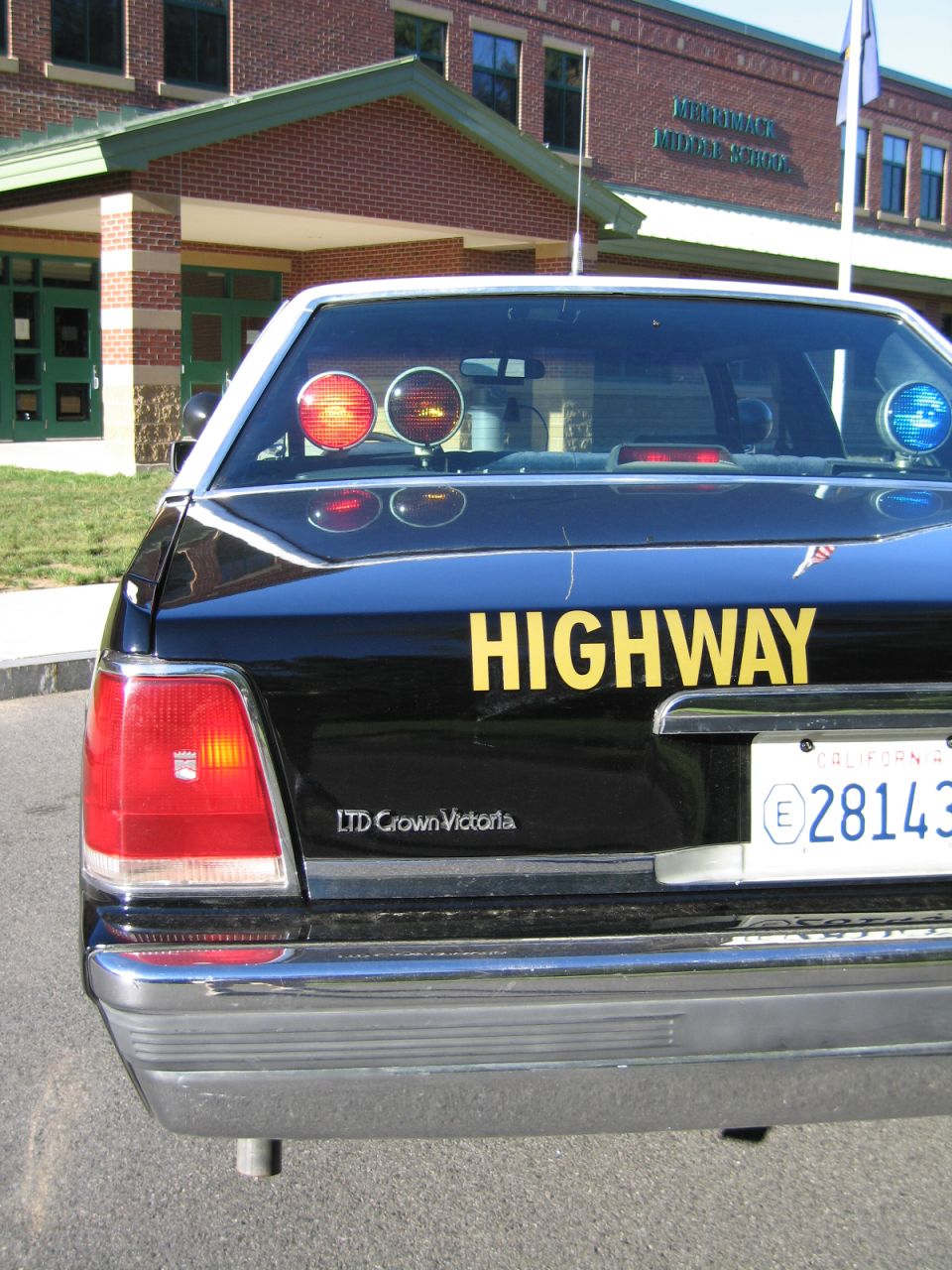 Rear of black police sedan with yellow HIGHWAY lettering and LTD Crown Victoria badge