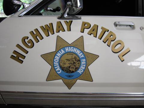 1991 Ford LTD Crown Victoria - Close-up of a white police car door showing arched HIGHWAY PATROL lettering and the gold California Highway Patrol star emblem.