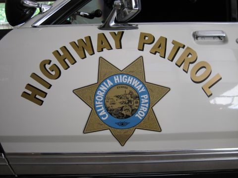1991 Ford LTD Crown Victoria - White police car door detailed with arched gold HIGHWAY PATROL lettering and a California Highway Patrol star emblem with chrome trim.