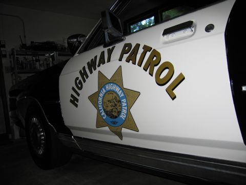 1991 Ford LTD Crown Victoria - Angled view of a white police car door with HIGHWAY PATROL lettering and a California Highway Patrol star emblem, parked in a garage.