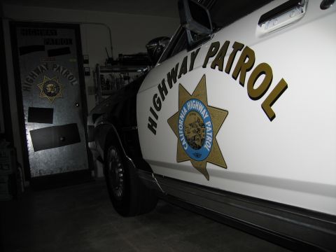 1991 Ford LTD Crown Victoria - White police car door bearing HIGHWAY PATROL lettering and the CHP star, with the matching emblem door visible in the garage behind it.