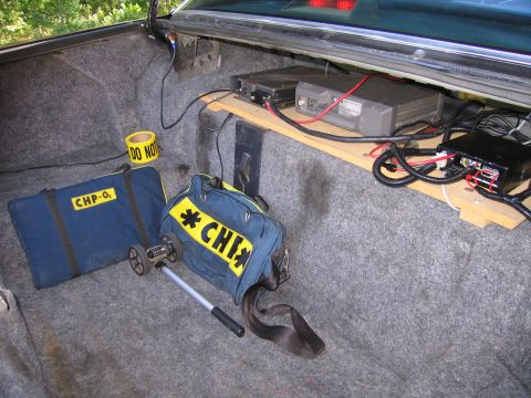 1991 Ford LTD Crown Victoria - Vehicle trunk packed with mounted radio equipment, loose wiring, caution tape and navy CHP-labeled duffel bags.