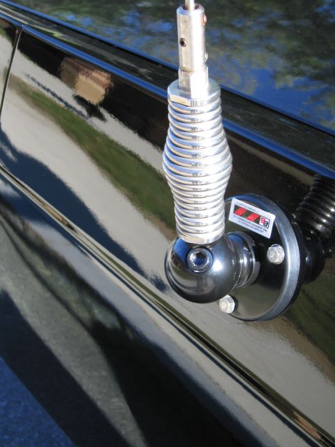 1991 Ford LTD Crown Victoria - Close-up of a chrome coil-spring whip antenna mounted on the glossy black rear quarter panel of a car.