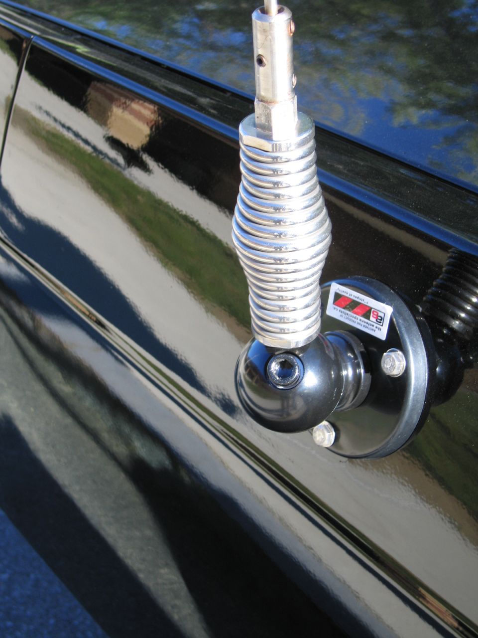 Chrome coil-spring whip antenna mounted on a glossy black car body panel