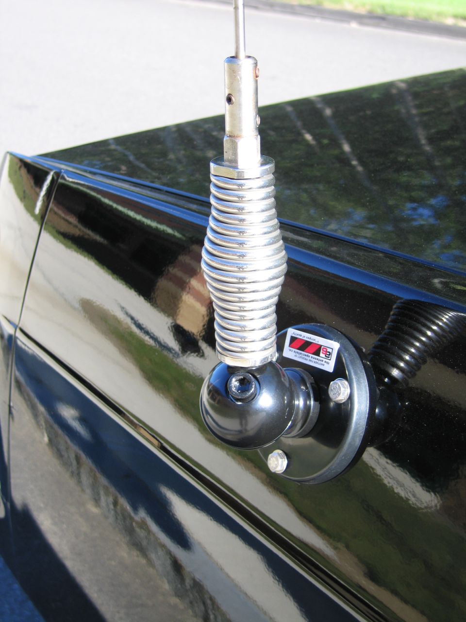 Chrome spring-base whip antenna mounted on a glossy black car panel
