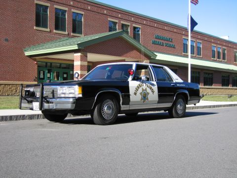 1991 Ford LTD Crown Victoria - Black-and-white California Highway Patrol Ford sedan with a push bumper parked in front of a brick middle school building.