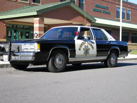 1991 Ford LTD Crown Victoria - black-and-white police sedan lettered Highway Patrol with a star emblem sits parked in front of the brick Merrimack Middle School building.