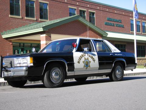 1991 Ford LTD Crown Victoria - Front three-quarter view of a black-and-white Highway Patrol police sedan parked beside the Merrimack Middle School entrance under a flagpo…