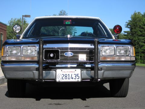 1991 Ford LTD Crown Victoria - Head-on view of a dark Ford police sedan fitted with a black push bar, spotlight and roof beacon, wearing California plate 281435.