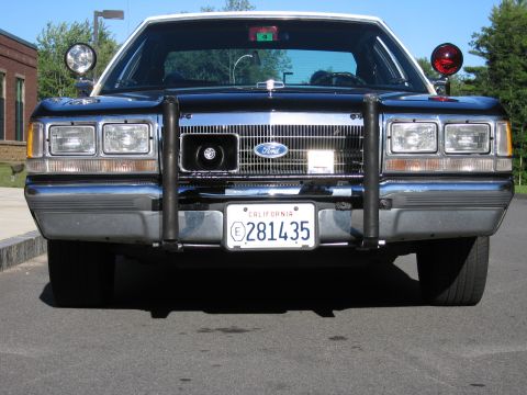 1991 Ford LTD Crown Victoria - Close front view of a Ford police sedan grille with brush guard, twin headlights and a California exempt plate reading 281435.
