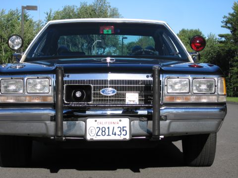 1991 Ford LTD Crown Victoria - Head-on view of a dark blue-black Ford police sedan with chrome grille, spotlight and roof beacon, plate California 281435.