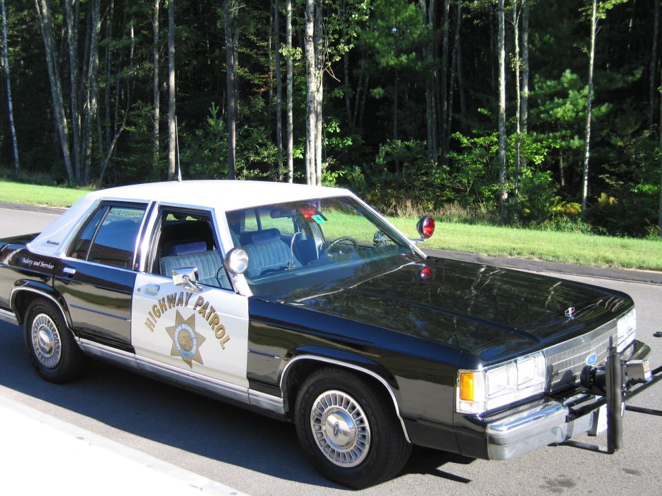 Front-quarter view of black-and-white Highway Patrol police sedan at roadside