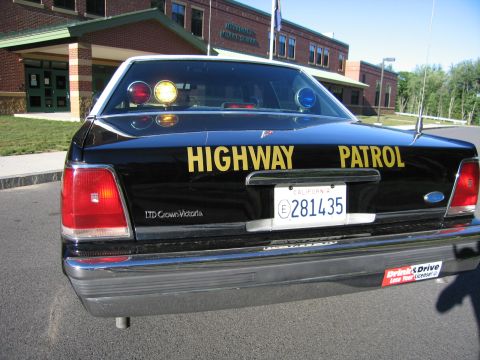 1991 Ford LTD Crown Victoria - Rear view of a black Ford LTD Crown Victoria lettered Highway Patrol with roof lights and California plate 281435, parked at a brick school.