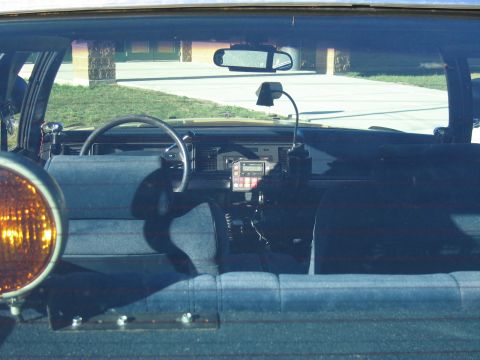1991 Ford LTD Crown Victoria - Interior of a police car seen through the windshield, with steering wheel, mounted radio gear, an amber light and gray bench seats.