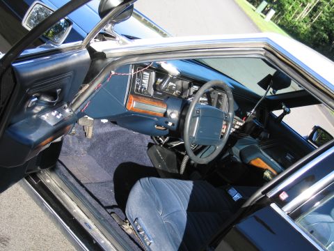 1991 Ford LTD Crown Victoria - Through the open door, a police car interior with blue cloth seats, woodgrain dash, steering wheel and dash-mounted equipment is visible.