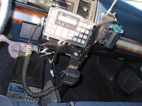 1991 Ford LTD Crown Victoria - console-mounted two-way radio control head with coiled-cord microphone and additional electronics installed in a police car with woodgrain…