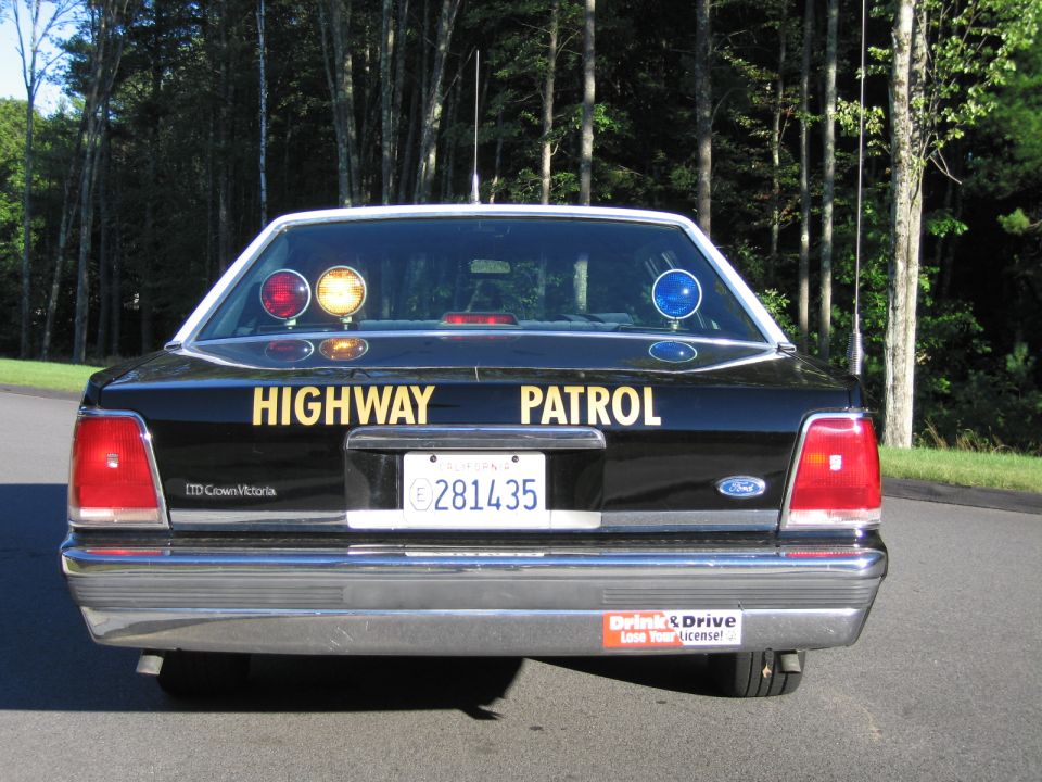 Rear view of black Ford LTD Crown Victoria patrol car with warning lights illuminated