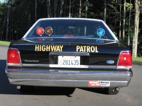 1991 Ford LTD Crown Victoria - Black Ford LTD Crown Victoria police sedan photographed from a low rear angle with HIGHWAY PATROL lettering and warning lights.