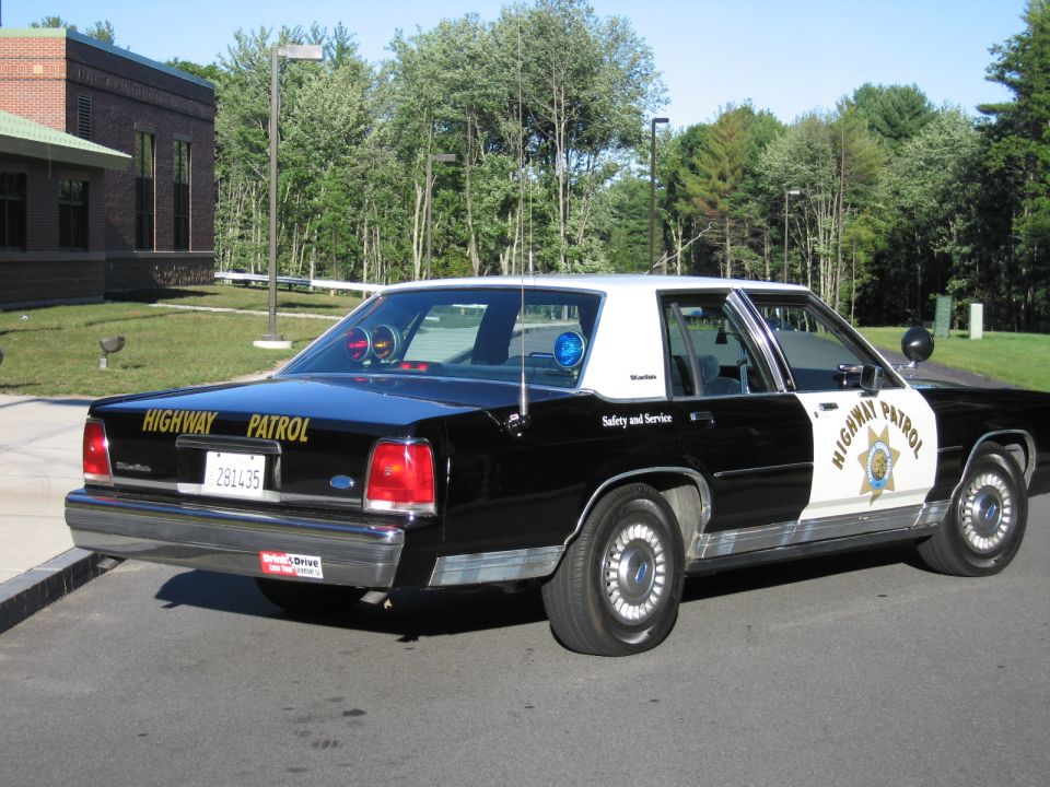 Black-and-white Ford Crown Victoria highway patrol sedan with door star, rear angle