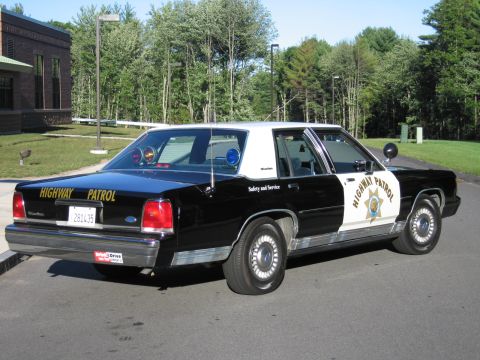 1991 Ford LTD Crown Victoria - Black-and-white Ford LTD Crown Victoria police sedan, rear three-quarter view, with a gold door star and HIGHWAY PATROL markings.