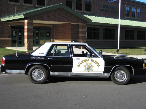 1991 Ford LTD Crown Victoria - Black-and-white Ford LTD Crown Victoria patrol car shown in passenger-side profile with gold seven-point door star and HIGHWAY PATROL lette…