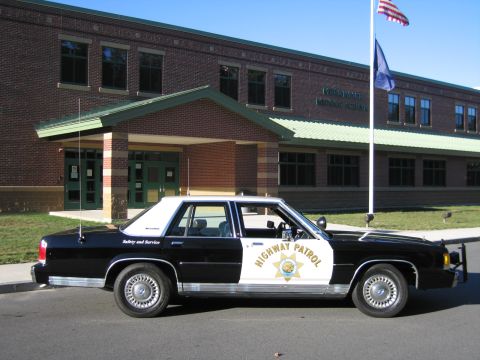 1991 Ford LTD Crown Victoria - Driver-side profile of a black-and-white Ford LTD Crown Victoria patrol car with HIGHWAY PATROL door star, parked outside a brick building.