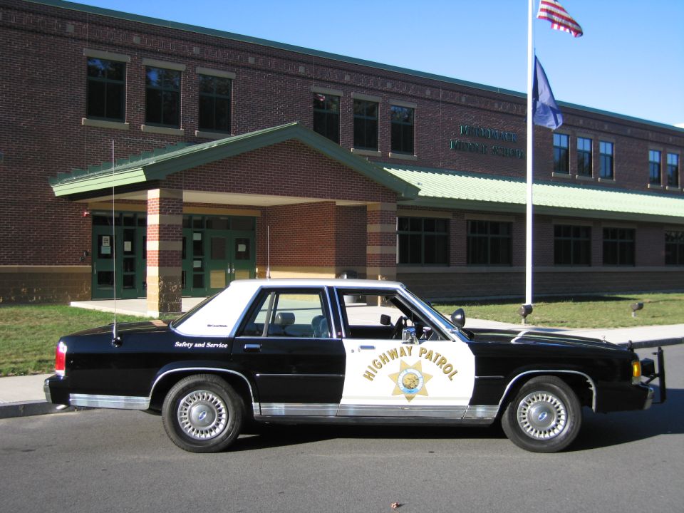 Driver-side profile of black-and-white highway patrol Crown Victoria by brick building