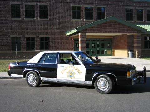 1991 Ford LTD Crown Victoria - Black-and-white Ford LTD Crown Victoria police sedan, passenger-side three-quarter view, with door star and HIGHWAY PATROL markings.