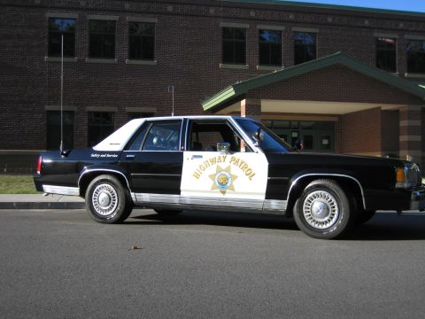 1991 Ford LTD Crown Victoria - Passenger-side profile of a black-and-white Ford LTD Crown Victoria patrol car with seven-point door star and HIGHWAY PATROL lettering.