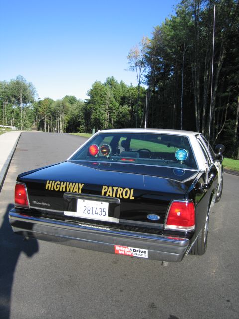 1991 Ford LTD Crown Victoria - Rear view of a black Ford LTD Crown Victoria police car with gold HIGHWAY PATROL lettering, rear-deck warning lights, and a tall whip anten…