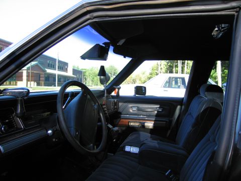 1991 Ford LTD Crown Victoria - Interior of a car showing the steering wheel, dashboard, a pillar-mounted spotlight, and patterned cloth front seats.