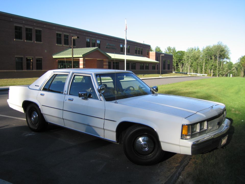 White Ford four-door sedan parked in front of a brick building