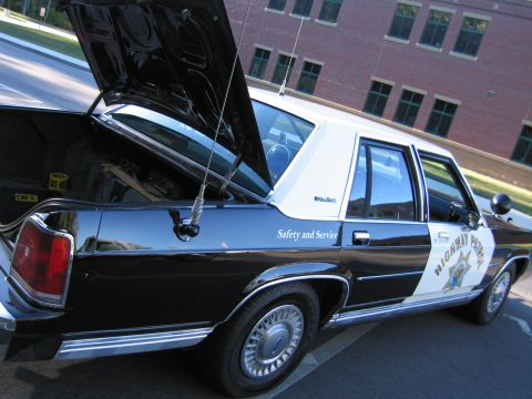 1991 Ford LTD Crown Victoria - Rear three-quarter view of a black-and-white Highway Patrol police sedan with its trunk and hood open near a brick building.