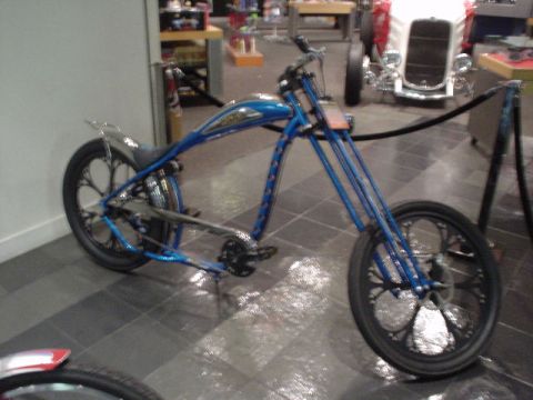 1968 Ford Mustang - A custom blue chopper motorcycle is displayed indoors, intricate spoke designs on its wheels and a long, low frame.