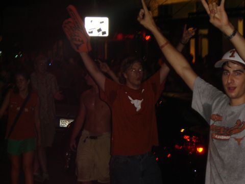 1988 Ford LTD Crown Victoria - A group of people celebrate outdoors at night, with one person holding a large foam finger and others raising their arms.