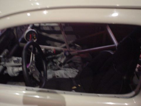 1968 Ford Mustang - The interior of a race car is visible through the window, showing a roll cage, racing seat, and dashboard gauges.