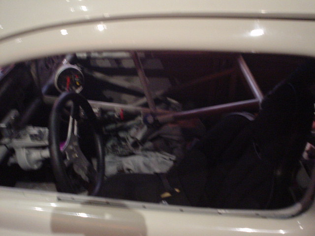 Interior view of a race car with a roll cage, racing seat, and gauges visible through the window