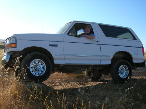 1994 Ford Bronco - A white 1994 Ford Bronco is seen from the side with a person driving it on a dirt path.