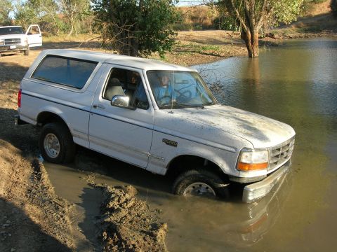 1994 Ford Bronco - White 1994 Ford Bronco is stuck in mud and water with another vehicle in the background.