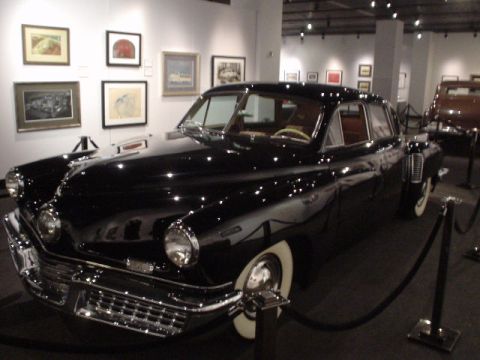 1968 Ford Mustang - A black sedan is displayed in a museum setting, with other vehicles and artwork visible.