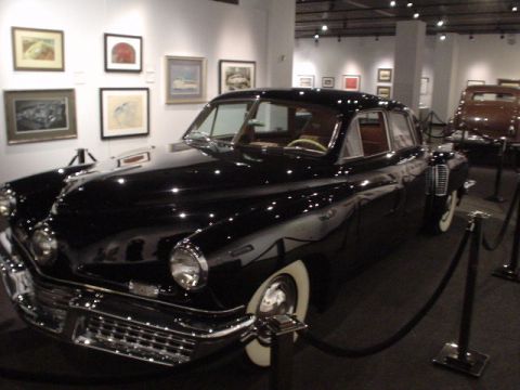 1968 Ford Mustang - A black sedan is displayed in a museum hall, with artwork visible on the walls and another car in the background.