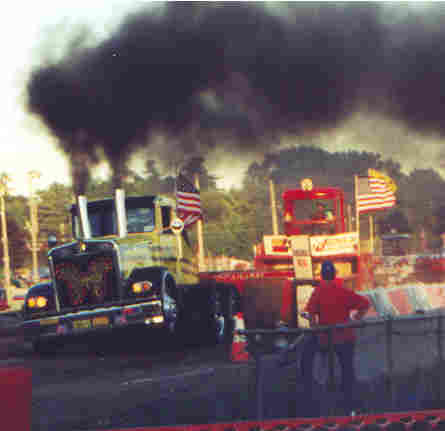 1994 Ford F-150 - Trucks compete in a pull event, kicking up large plumes of dark smoke.