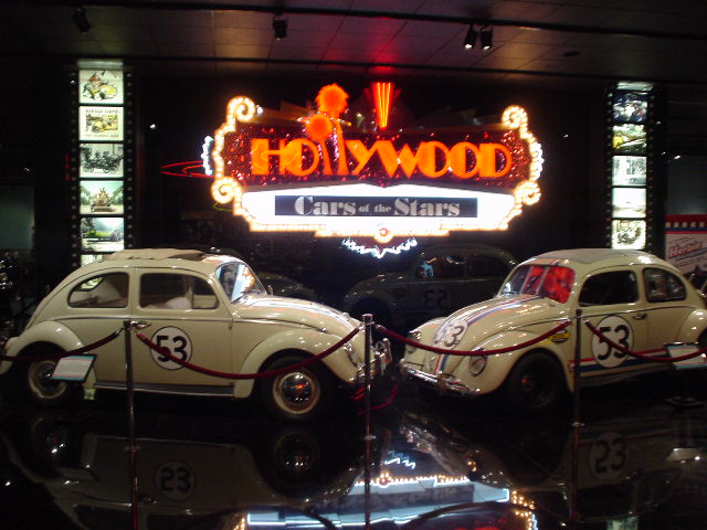 Two white Volkswagen Beetles with number 53 on the doors are displayed under a 'Hollywood Cars of the Stars' sign