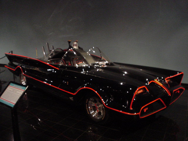 Black custom car with red trim, seen from a 3/4 front angle in a museum