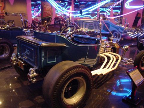 1968 Ford Mustang - A custom hot rod with a Ford emblem is displayed indoors with neon lights in the background.