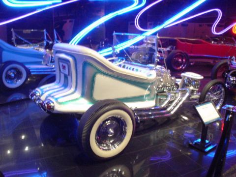 1968 Ford Mustang - A custom hot rod with distinctive paint and chrome is displayed alongside other vehicles under neon lights.